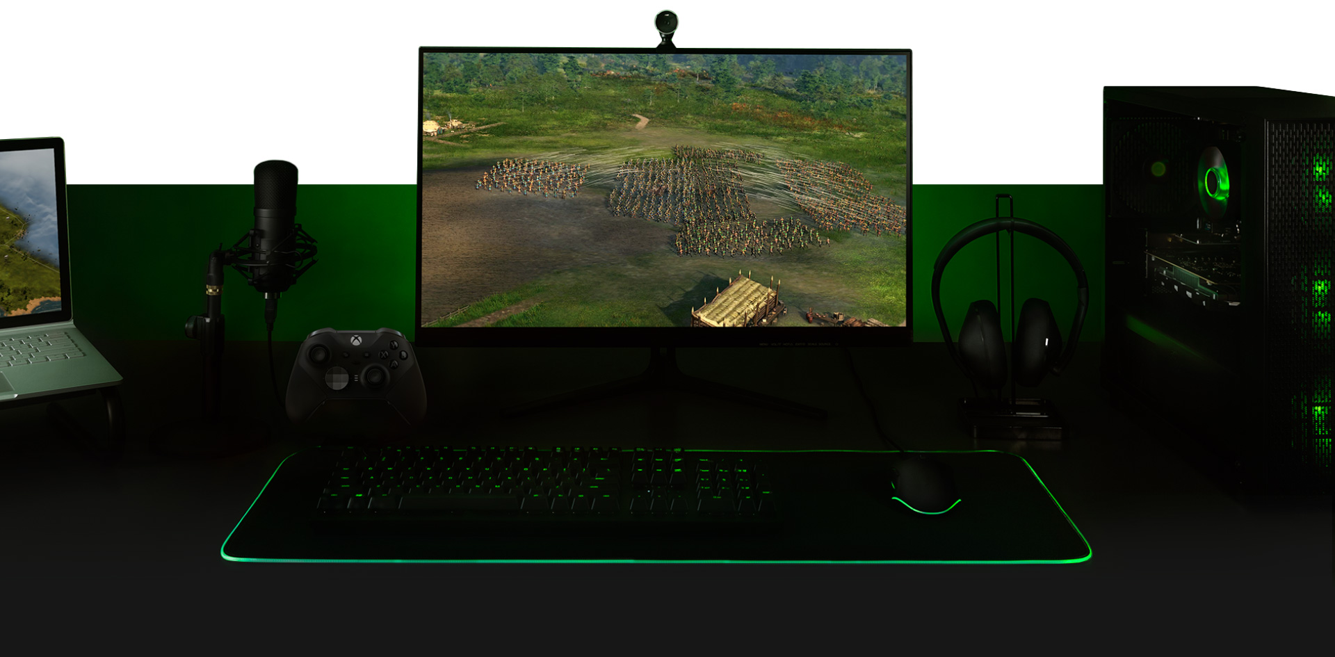 Desktop with a PC, monitor with Ara: History Untold game screen, keyboard, Xbox One controller, microphone and a laptop all set up together.